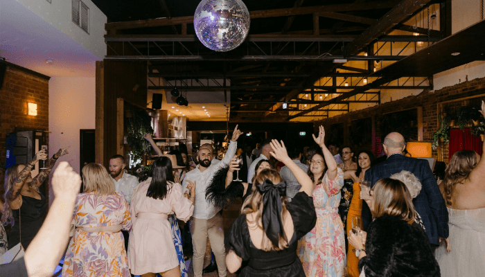 Guests dancing and celebrating at a Melbourne corporate event with a DJ creating a lively atmosphere under a disco ball