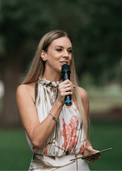 Alana With Love — Melbourne celebrant with microphone surrounded by flowers at outdoor ceremony