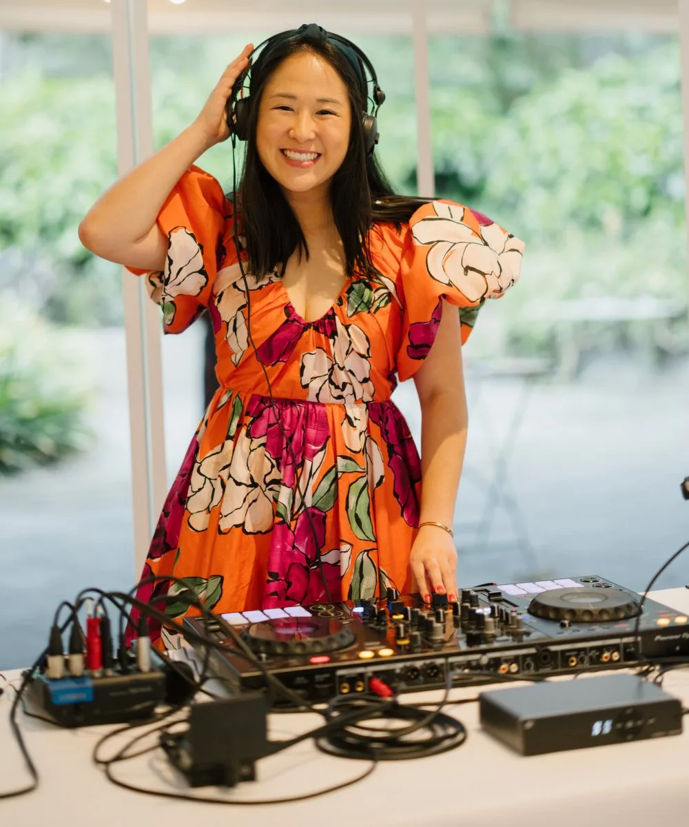 DJ Emily Gracie smiling at the decks in a floral dress — award-winning Melbourne wedding DJ