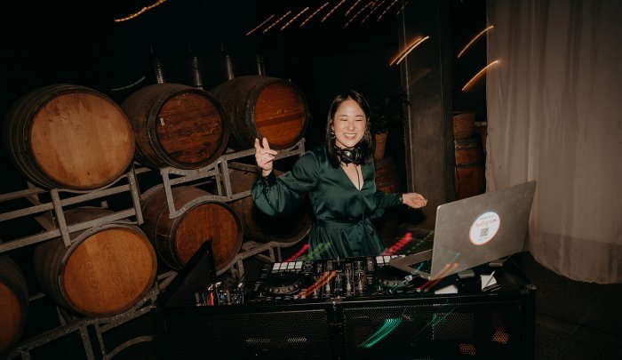 DJ Emily Gracie smiling at the decks in front of wine barrels at a Melbourne private function