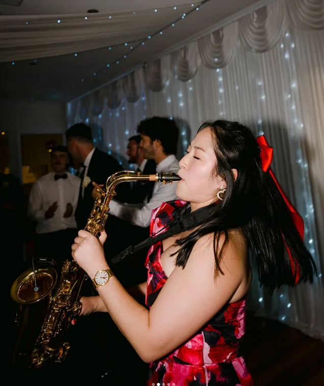 DJ Emily Gracie playing live saxophone at a wedding reception under fairy lights